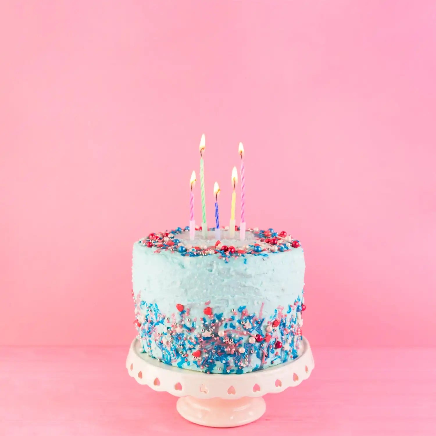 Un gâteau d'anniversaire bleu clair avec des confettis colorés et cinq bougies allumées sur le dessus.