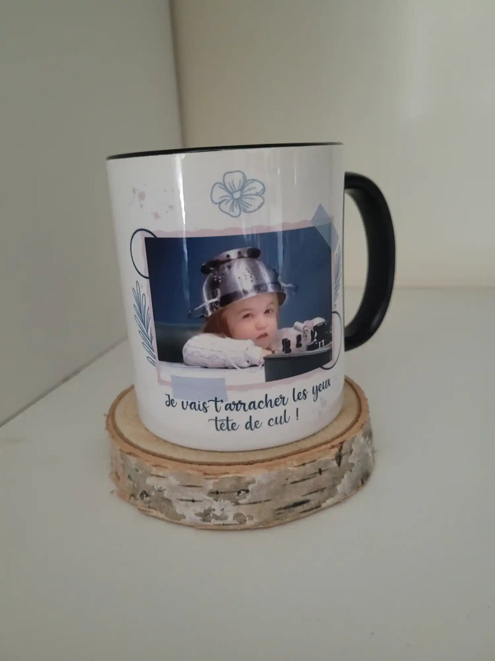 Une tasse en céramique blanche avec une poignée noire, présentant une image humoristique d'un bébé portant une casserole en métal comme casque et une phrase française en dessous.