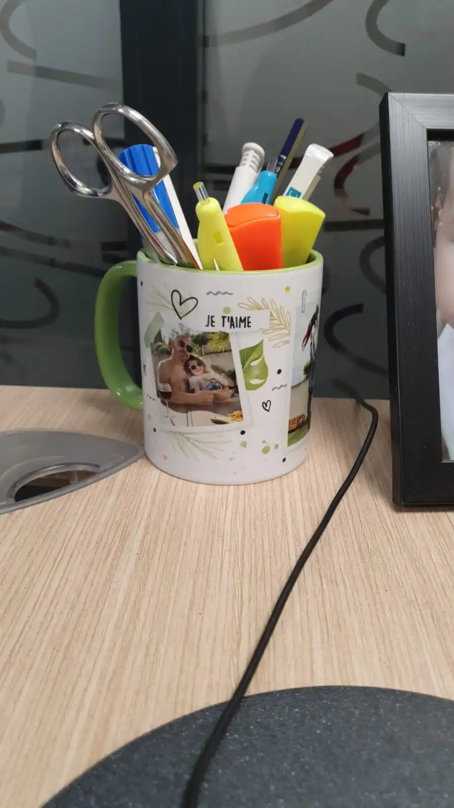 Une tasse en céramique blanche avec une poignée verte, remplie d'un assortiment de fournitures de bureau.