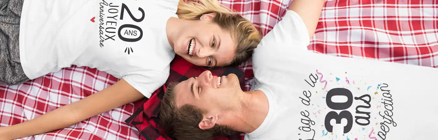 Deux personnes portant des t-shirts blancs avec des motifs d'anniversaire, allongées sur une couverture à carreaux rouge et blanc.