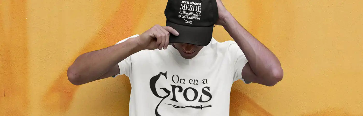 Une personne portant une casquette de baseball noire avec du texte blanc et un t-shirt blanc avec du texte noir.